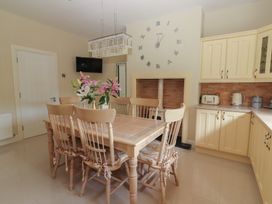 A kitchen dining area with a wooden table and six chairs a vase of flowers a wall clock a small tv and cream cabinets at Killelton Cottage Camp County Kerry