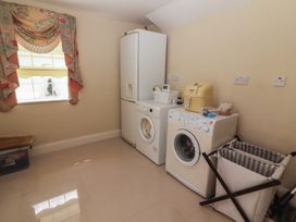 A laundry room with a washing machine, dryer, refrigerator, laundry basket, and a window with floral curtains at Killelton Cottage in Camp County Kerry