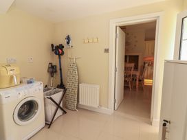 A utility room with a washing machine ironing board laundry basket and vacuum cleaners next to a doorway leading to a kitchen with wooden chairs at Killelton Cottage in Camp County Kerry