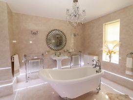 A bathroom with a freestanding bathtub a pedestal sink a round mirror and a window with flowers at Killelton Cottage Camp County Kerry