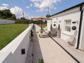 An outdoor patio with stone furniture including a table bench and chairs and an umbrella with plants along a white wall at Killelton Cottage in Camp County Kerry