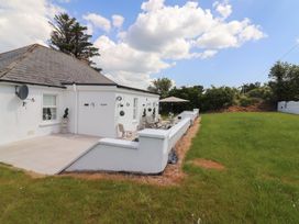 A white house with a patio and outdoor furniture next to a green lawn at Killelton Cottage Camp County Kerry