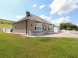 A bungalow house with a front porch and driveway surrounded by a grass lawn at Killelton Cottage in Camp County Kerry