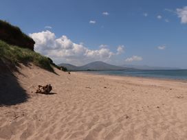 A sandy beach with grassy dunes on the left and mountains in the distance under a blue sky at Killelton Cottage in Camp County Kerry