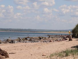 A sandy beach with rocks along the shore and water with a distant green landscape under a partly cloudy sky at Killelton Cottage in Camp County Kerry