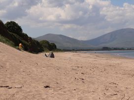 A sandy beach with scattered rocks and seaweed next to a grassy hillside with mountains in the background at Killelton Cottage in Camp County Kerry