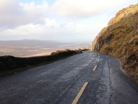A winding road along a hillside with a stone wall on the left and rocky terrain on the right at Killelton Cottage in Camp County Kerry