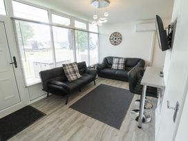 A living room with two black sofas a wall clock a mounted TV and bar stools at 99 Cherry Park in Chapel St Leonards