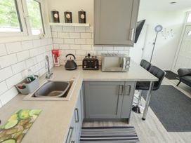 A kitchen with grey cabinets a sink a kettle microwave toaster and bar stools at 99 Cherry Park in Chapel St Leonards