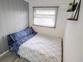 A bedroom with a bed with geometric patterned bedding under a window with blinds and a wall shelf with a plant and vase at 99 Cherry Park in Chapel St Leonards