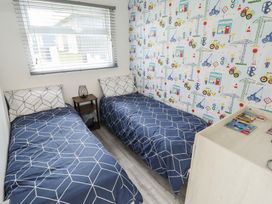 A bedroom with two single beds and a nightstand under a window at 99 Cherry Park in Chapel St Leonards