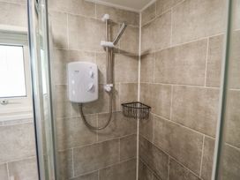 A shower area with a white electric shower unit a handheld showerhead and a corner wire shelf in a tiled bathroom at 99 Cherry Park in Chapel St Leonards