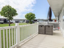 A porch with white railing a closed umbrella and two wicker storage boxes at 99 Cherry Park in Chapel St Leonards