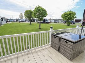 A porch with a wicker table and white railing overlooking a green lawn with trees and parked vehicles at 99 Cherry Park in Chapel St Leonards