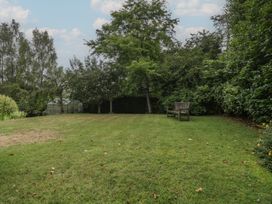 A garden with grass, trees, a bench and a greenhouse at St. Marys House Church Westcote near Bledington