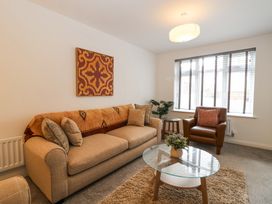 A living room with a beige sofa, leather armchair, glass coffee table, side table, plant, and window blinds at Peninsula Cottages - The Tors in Tavistock