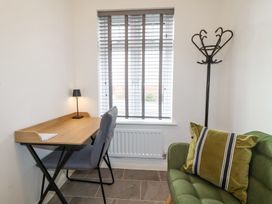 A small room with a wooden desk and chair beside a window with blinds a floor lamp a green sofa with a pillow and a black coat rack at Peninsula Cottages - The Tors in Tavistock
