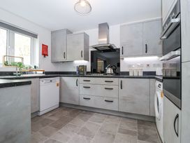 A kitchen with grey cabinets a dishwasher a washing machine a stove with kettle and a window at Peninsula Cottages - The Tors in Tavistock