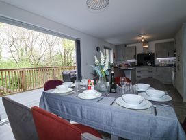 A dining table set with dishes and glasses in a kitchen with an open door to a wooden balcony with trees outside at Peninsula Cottages - The Tors in Tavistock
