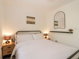 A bedroom with a bed, two bedside tables with lamps, a wall mirror, a painting, and a shelf with flowers at Peninsula Cottages - The Tors in Tavistock