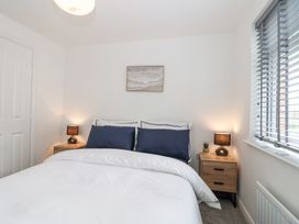 A bedroom with a bed with blue pillows two wooden bedside tables with lamps and a window with blinds at Peninsula Cottages - The Tors in Tavistock