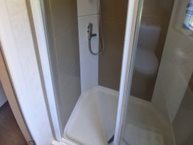 A shower with a showerhead and tiled wall at Emma No.6 in Llandegfan