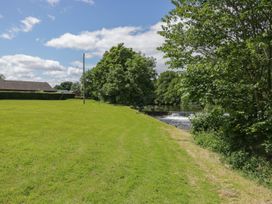 A grassy area next to a river with trees and a house at Bungalow 15 Eamont Park Penrith