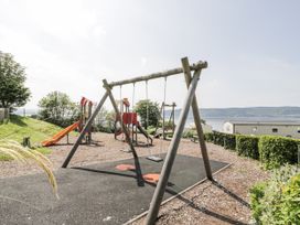 A playground with swings and a slide overlooking a water body at Number 42 Wemyss Bay