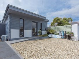 A gravel front yard with two surfboards plants and white chairs outside a gray and white building at Two Bare Feet Rose near Perranporth