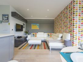 A living room with a white sectional sofa and colorful leaf patterned wallpaper at Two Bare Feet Rose near Perranporth
