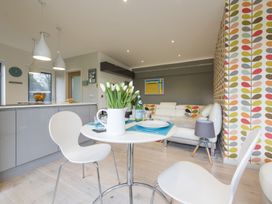 A modern open plan kitchen and living area with a small round dining table and white chairs at Two Bare Feet in Rose near Perranporth