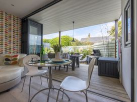 An indoor dining area with a round table and chairs opening to a covered outdoor patio with a grill and outdoor furniture at Two Bare Feet Rose near Perranporth