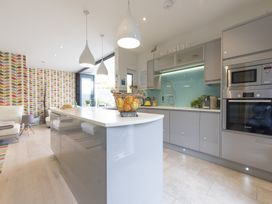 A modern kitchen with a central island white countertops grey cabinets and patterned wallpaper at Two Bare Feet Rose near Perranporth