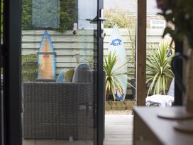An outdoor patio area with wicker furniture surfboards and potted plants at Two Bare Feet Rose near Perranporth