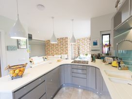 A kitchen with curved counter, grey cabinets, white pendant lights, and a living room with patterned wallpaper at Two Bare Feet in Rose near Perranporth
