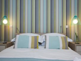 A bedroom with a double bed two striped pillows striped wallpaper and two bedside lamps at Two Bare Feet Rose near Perranporth
