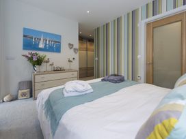 A bedroom with a bed a dresser with flowers and decor and striped wallpaper at Two Bare Feet in Rose near Perranporth
