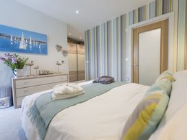 A bedroom with a bed, colorful striped wallpaper, a dresser with decorations, and a door at Two Bare Feet Rose near Perranporth