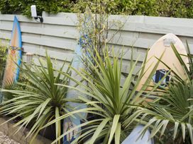A garden area with plants and three surfboards leaning against a wooden fence at Two Bare Feet Rose near Perranporth