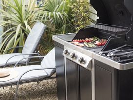 An outdoor area with a gas barbecue grill cooking vegetables and prawns next to lounge chairs and plants at Two Bare Feet in Rose near Perranporth