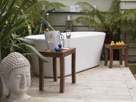 An outdoor bathtub with two wooden tables holding champagne glasses rubber ducks and a Buddha head statue at Two Bare Feet in Rose near Perranporth