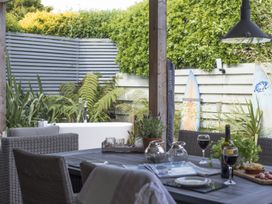 An outdoor dining area with wicker chairs a wooden table with wine glasses food plants and a bathtub with surfboards behind a wooden fence at Two Bare Feet Rose near Perranporth