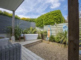 An outdoor space with a white bathtub on a wooden platform two surfboards plants and a wicker chair at Two Bare Feet Rose near Perranporth