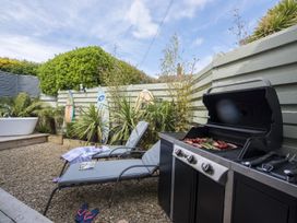 An outdoor patio area with a barbecue grill cooking food two lounge chairs surfboards and plants at Two Bare Feet in Rose near Perranporth