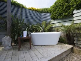 An outdoor bathtub on a wooden deck with plants and a small table holding a bottle and glasses at Two Bare Feet Rose near Perranporth