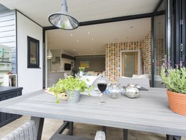 An outdoor dining table with plants and a glass of wine looking into a living area with patterned wallpaper at Two Bare Feet in Rose near Perranporth