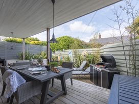 An outdoor covered patio with dining table and chairs a barbecue grill and lounge chairs at Two Bare Feet Rose near Perranporth