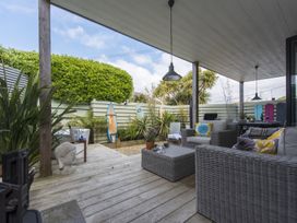 A covered patio with wicker furniture cushions surfboards and potted plants at Two Bare Feet Rose near Perranporth