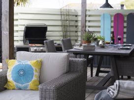An outdoor seating area with wicker chairs a table with plants and wine glasses and a barbecue grill at Two Bare Feet in Rose near Perranporth