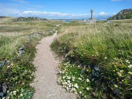 A pathway leading to a cross surrounded by grass and flowers at Hen Siop in Niwbwrch (newborough)